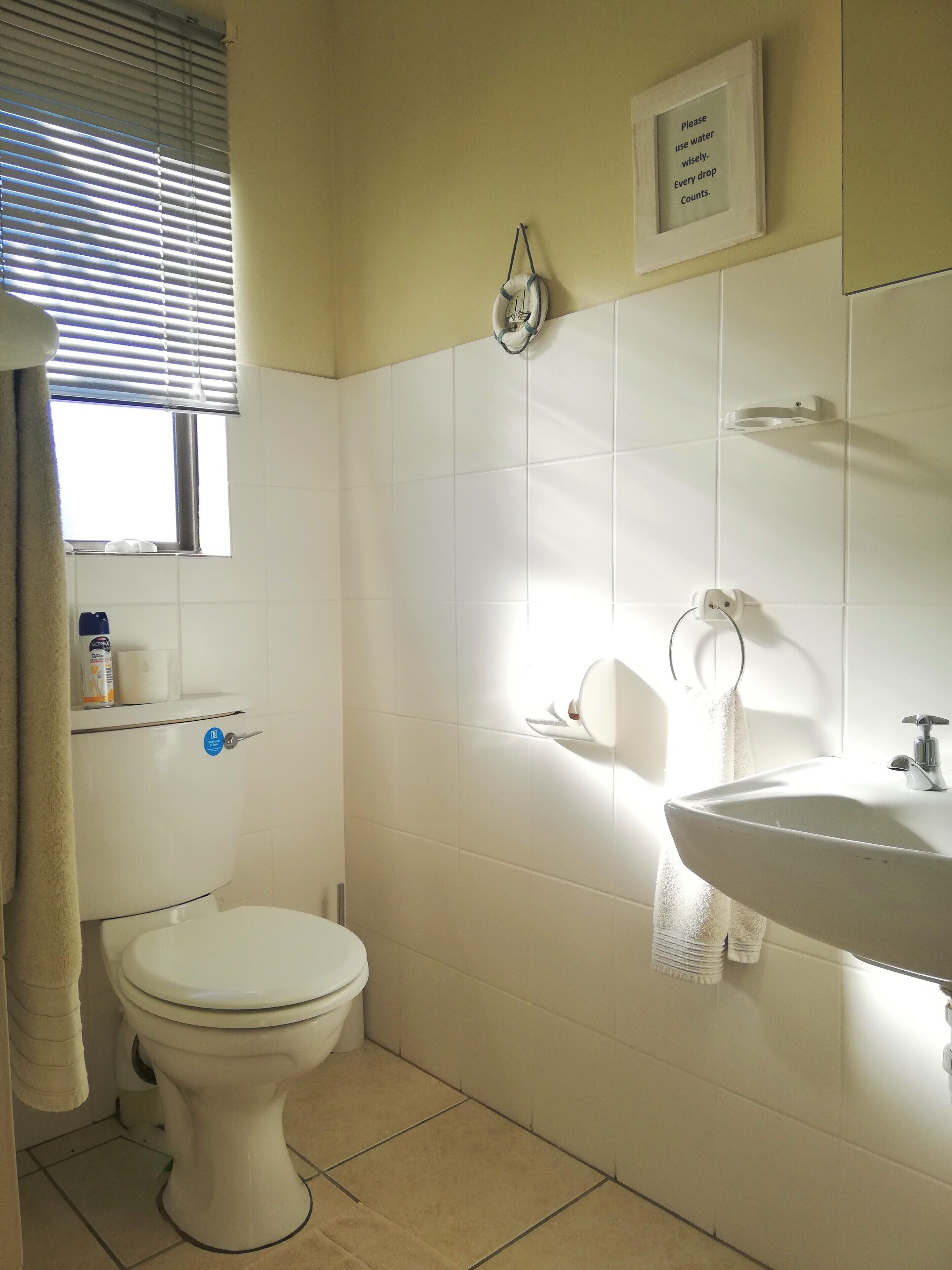 A bathroom with a toilet, sink, and a window with blinds.