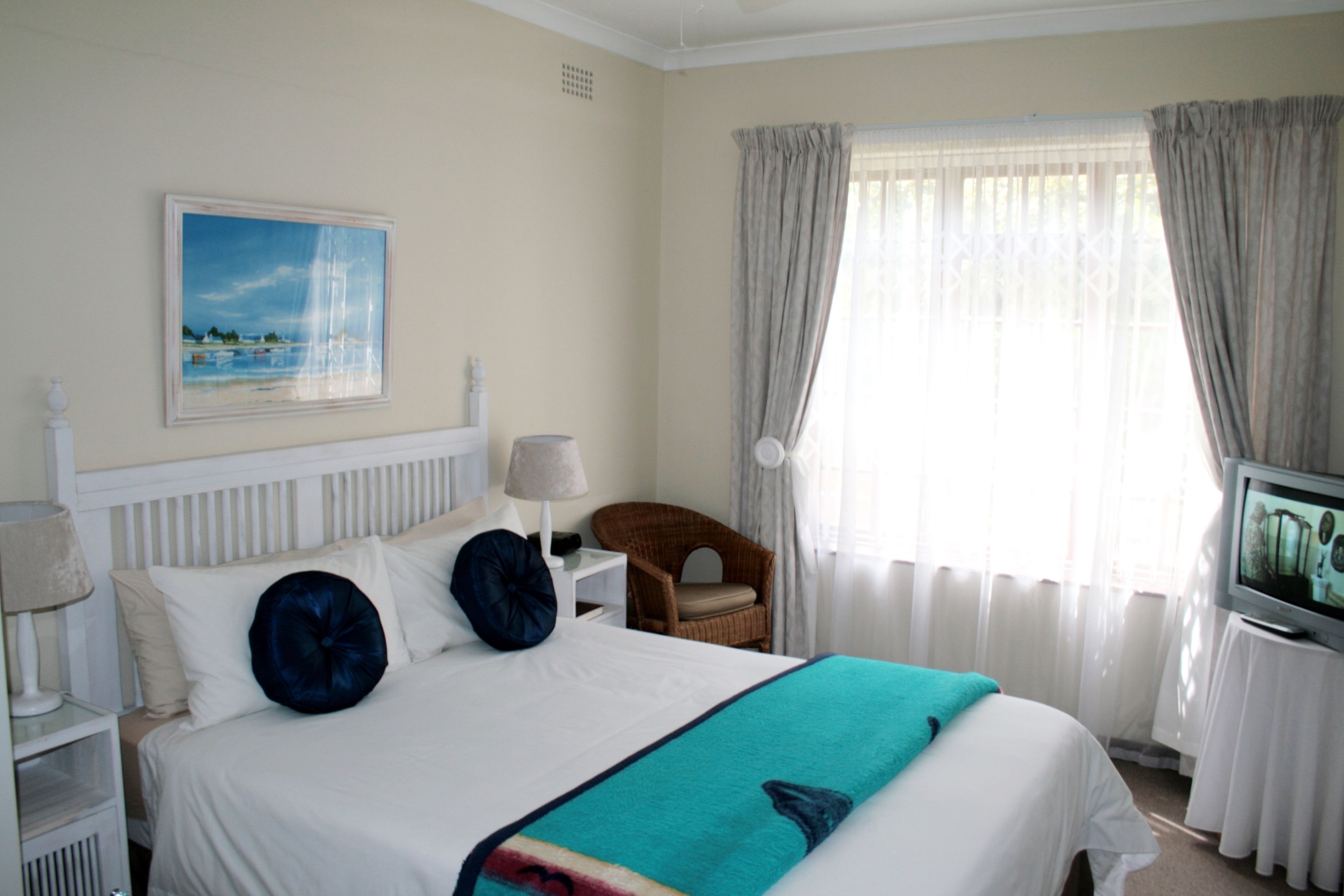 A hotel room with a bed, a television, a chair, a nightstand, and a painting on the wall.