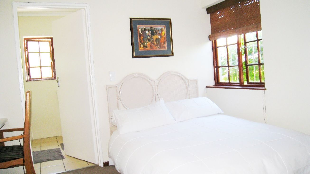 A bedroom with a bed, a door, a window, and a painting on the wall.