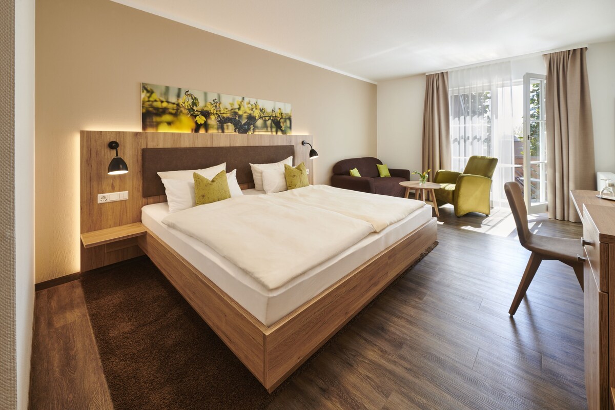 Una habitación de hotel con una cama grande, un escritorio, dos sillas y una ventana con cortinas.