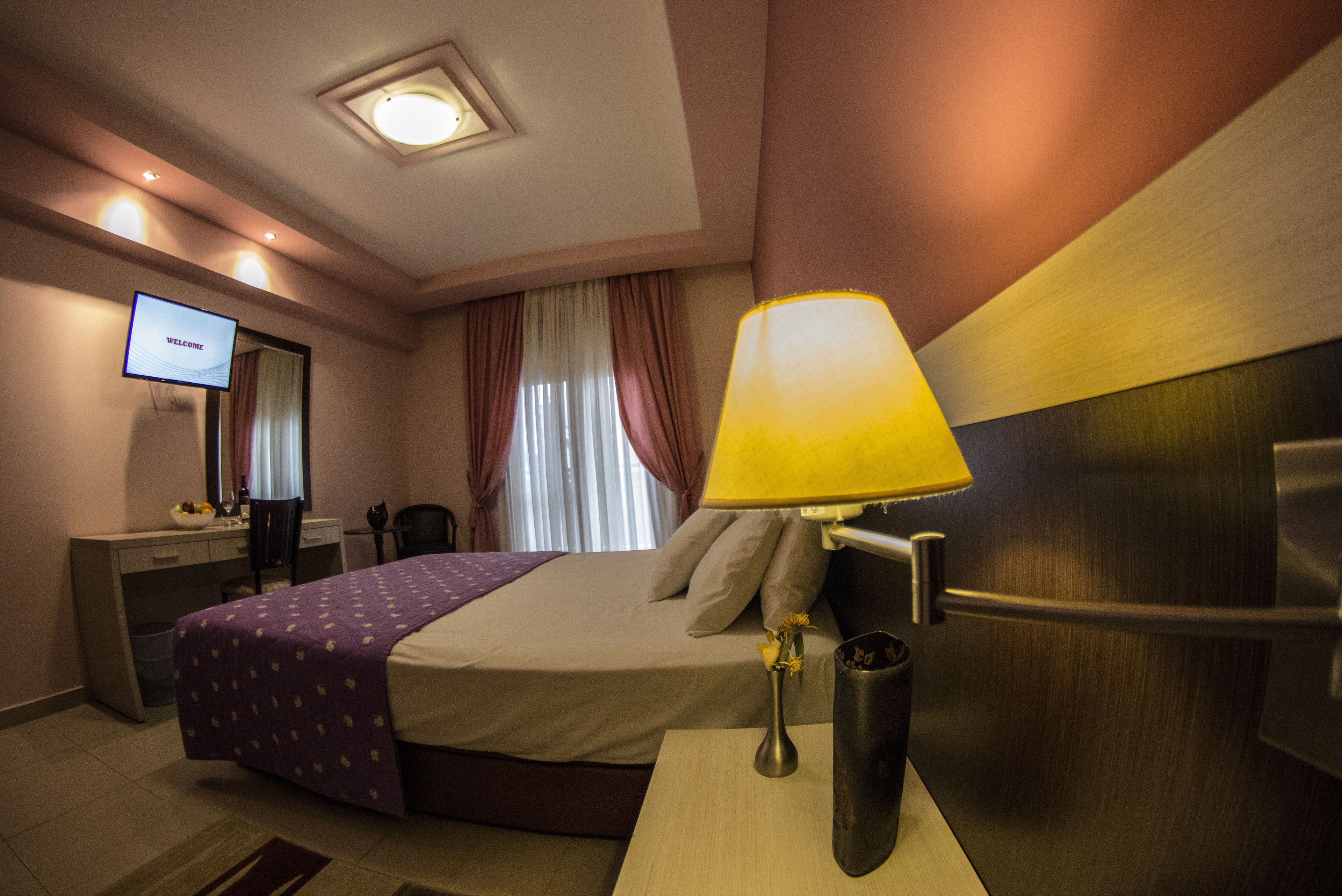 A hotel room with a bed, a desk, a TV, a lamp, and a window with curtains.