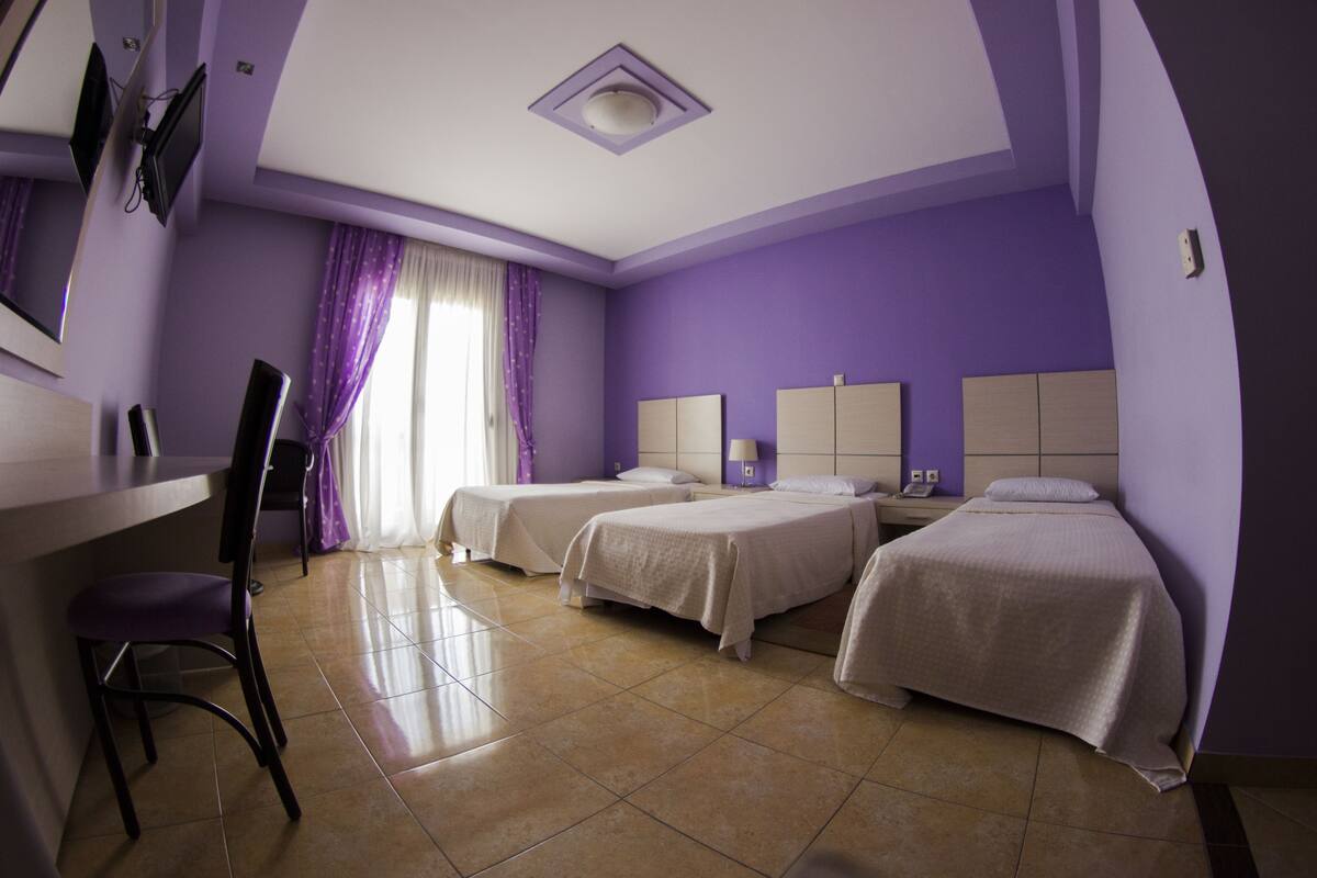 A hotel room with two beds, a desk with a chair, and a TV mounted on the wall.