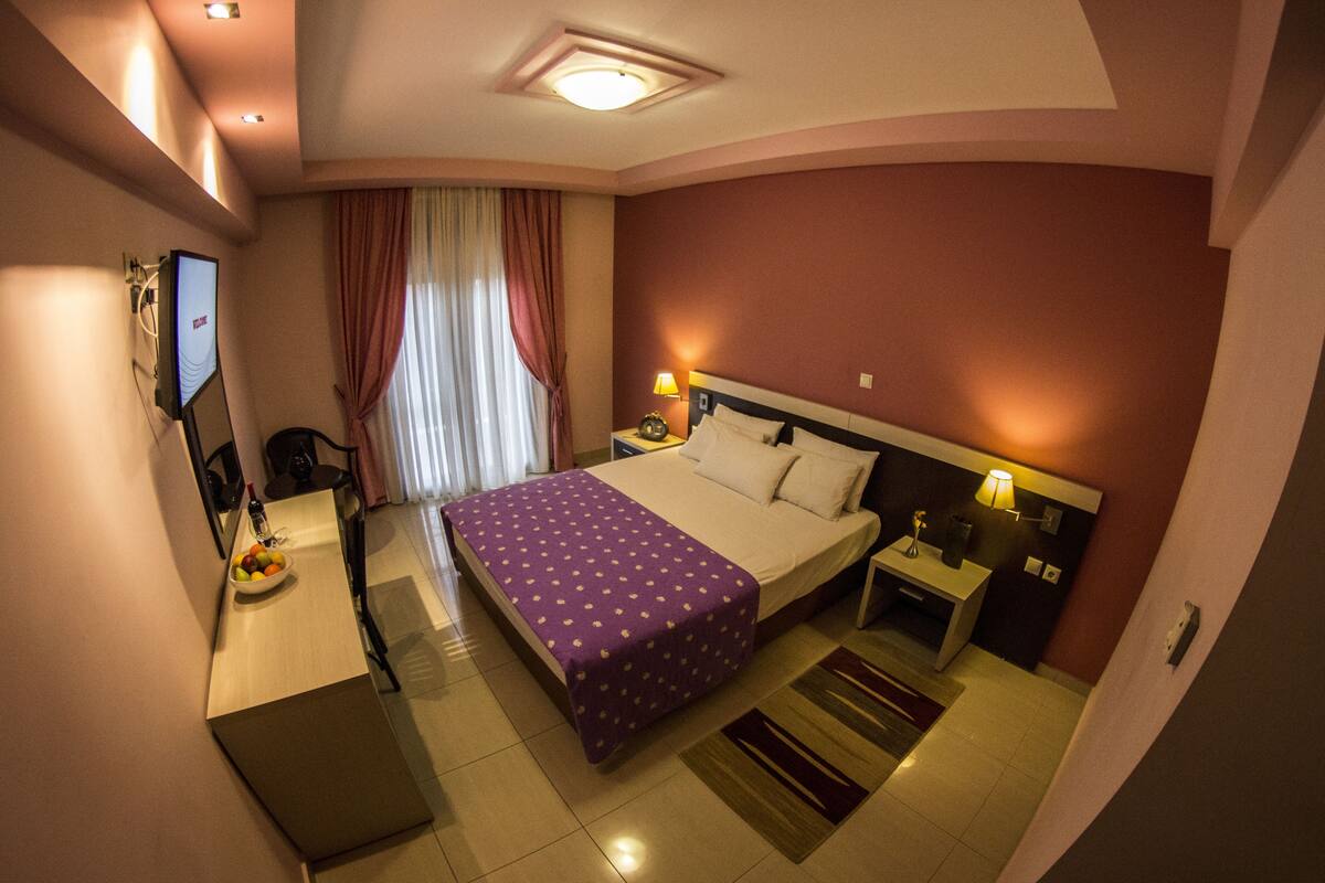A hotel room with a bed, bedside tables, a desk with a chair, a television, and a window with curtains.