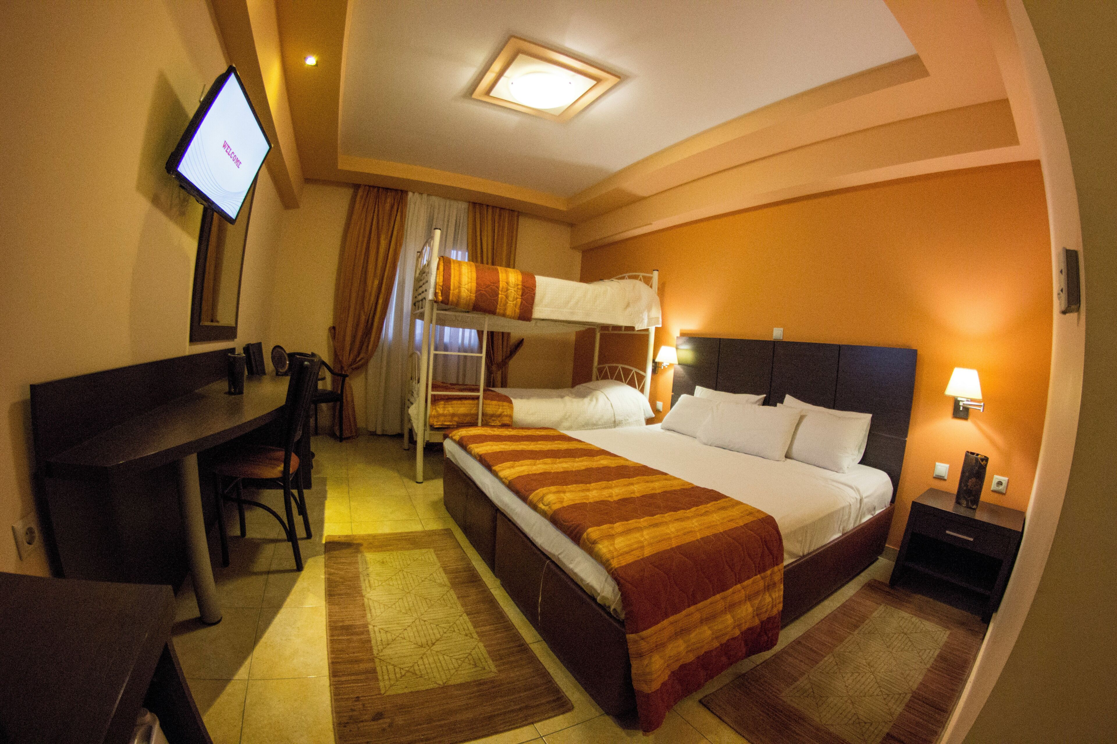 Una camera d'albergo con un letto a castello, una scrivania con sedia, una televisione e un comodino con lampada.