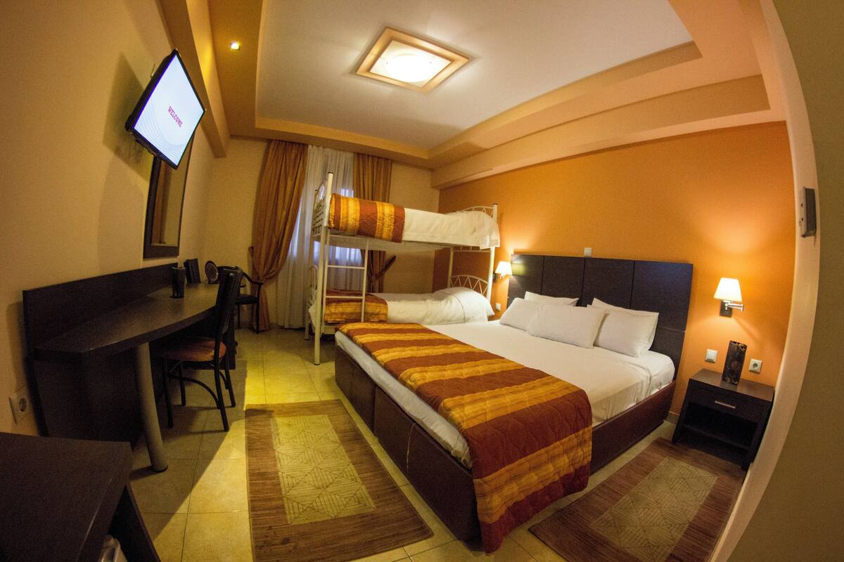 A hotel room with a bunk bed, a desk with a chair, a television, and a nightstand with a lamp.