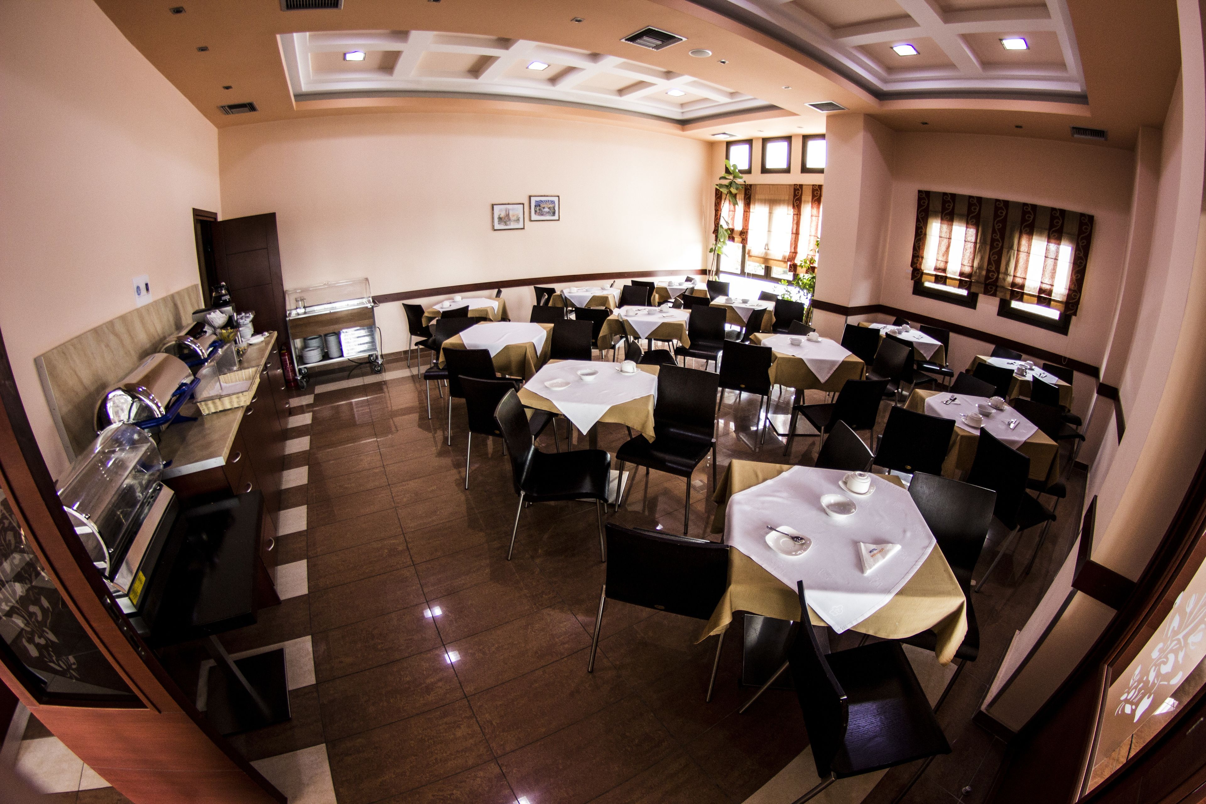 Comedor de hotel con varias mesas y sillas, una barra de buffet y un techo decorativo.
