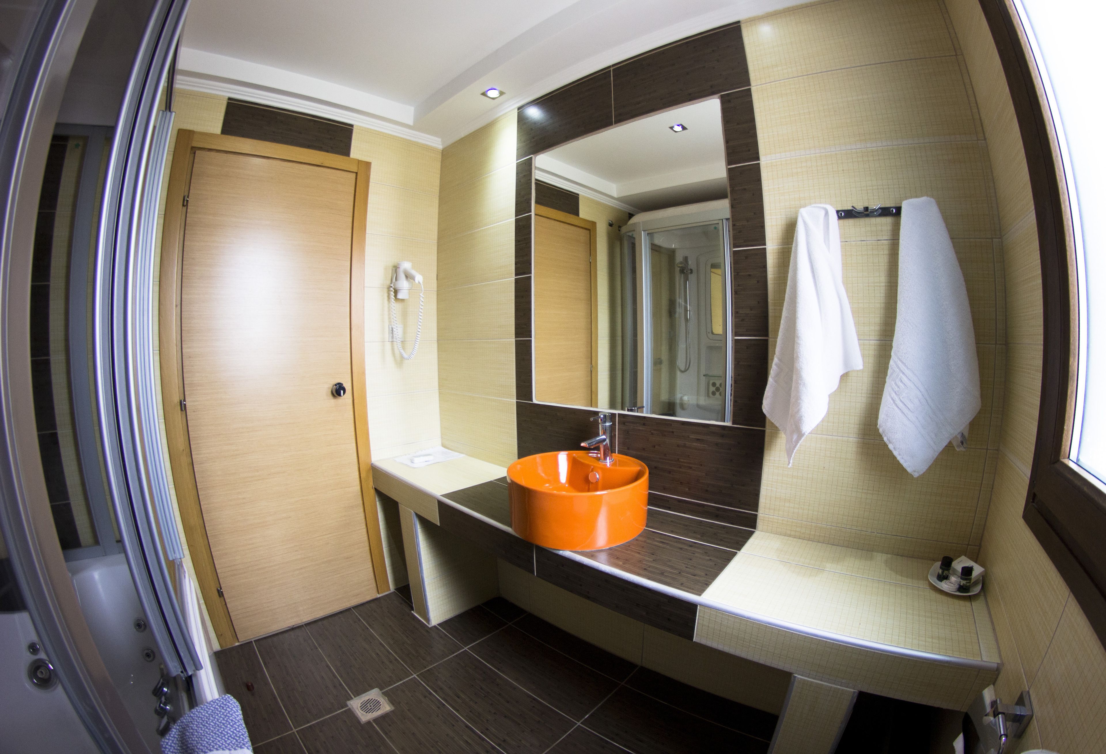 Een moderne badkamer met een houten deur, een douchecabine van glas en een wastafel met een oranje waskom.