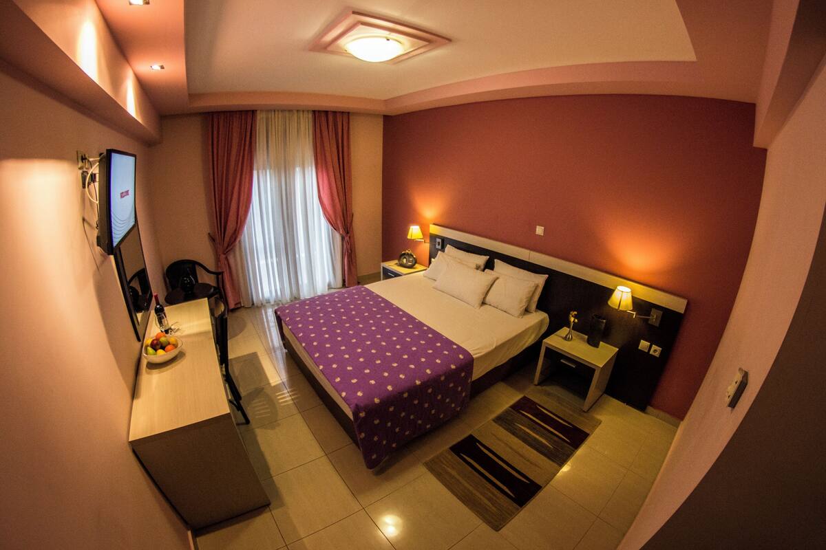 A hotel room with a bed, bedside tables, a TV, a desk with a chair, and a dining table with chairs.