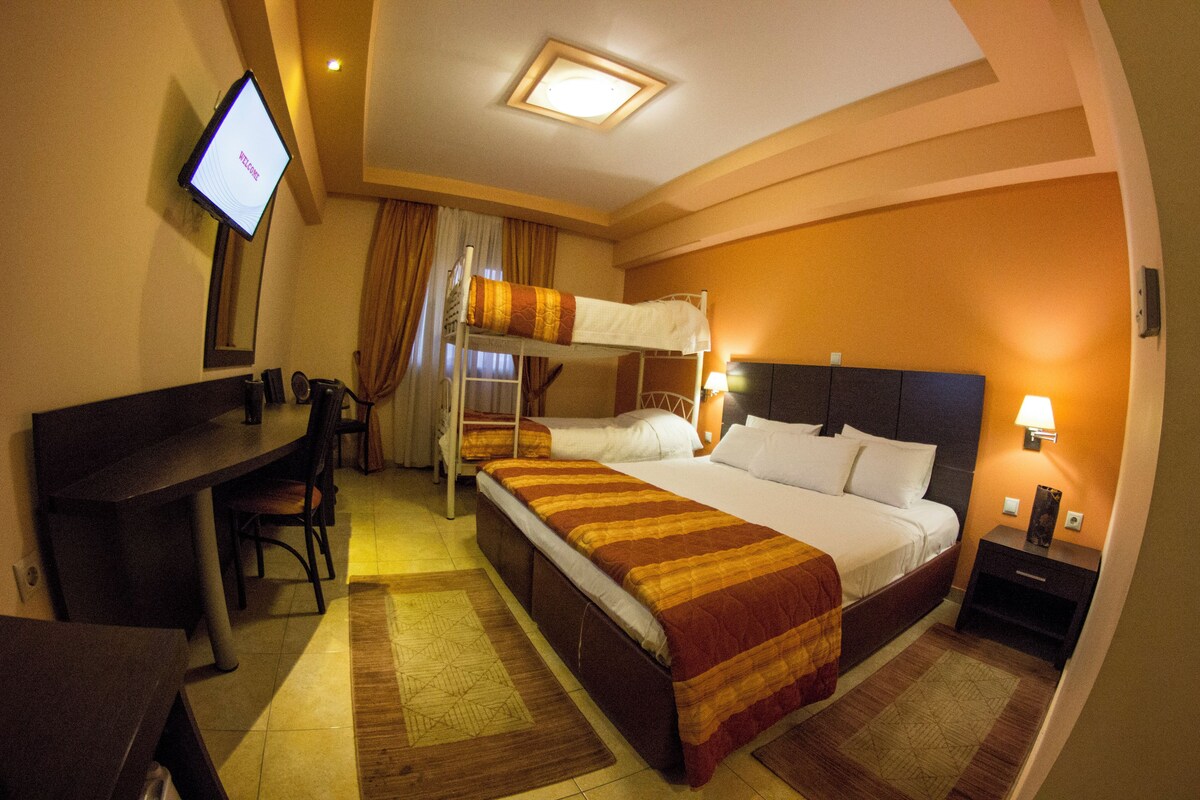 A hotel room with a bunk bed, a desk with a chair, a television, and a nightstand with a lamp.