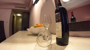 A table with a wine bottle and an empty wine glass, a bowl of fruit, and a television in the background.