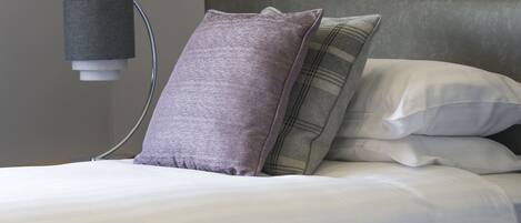 Una cama bien hecha con cabecera gris, ropa de cama blanca y almohada morada.