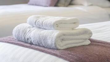 A neatly made bed with white linens and a folded white towel on a purple blanket.