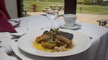 A dining table with a plate of food, a glass of wine, and a cup.