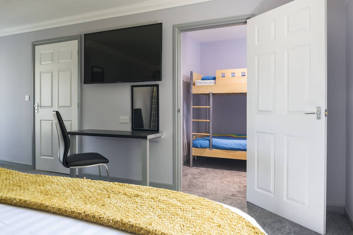 A bedroom with a bed, a desk with a chair, a TV, and a bunk bed.