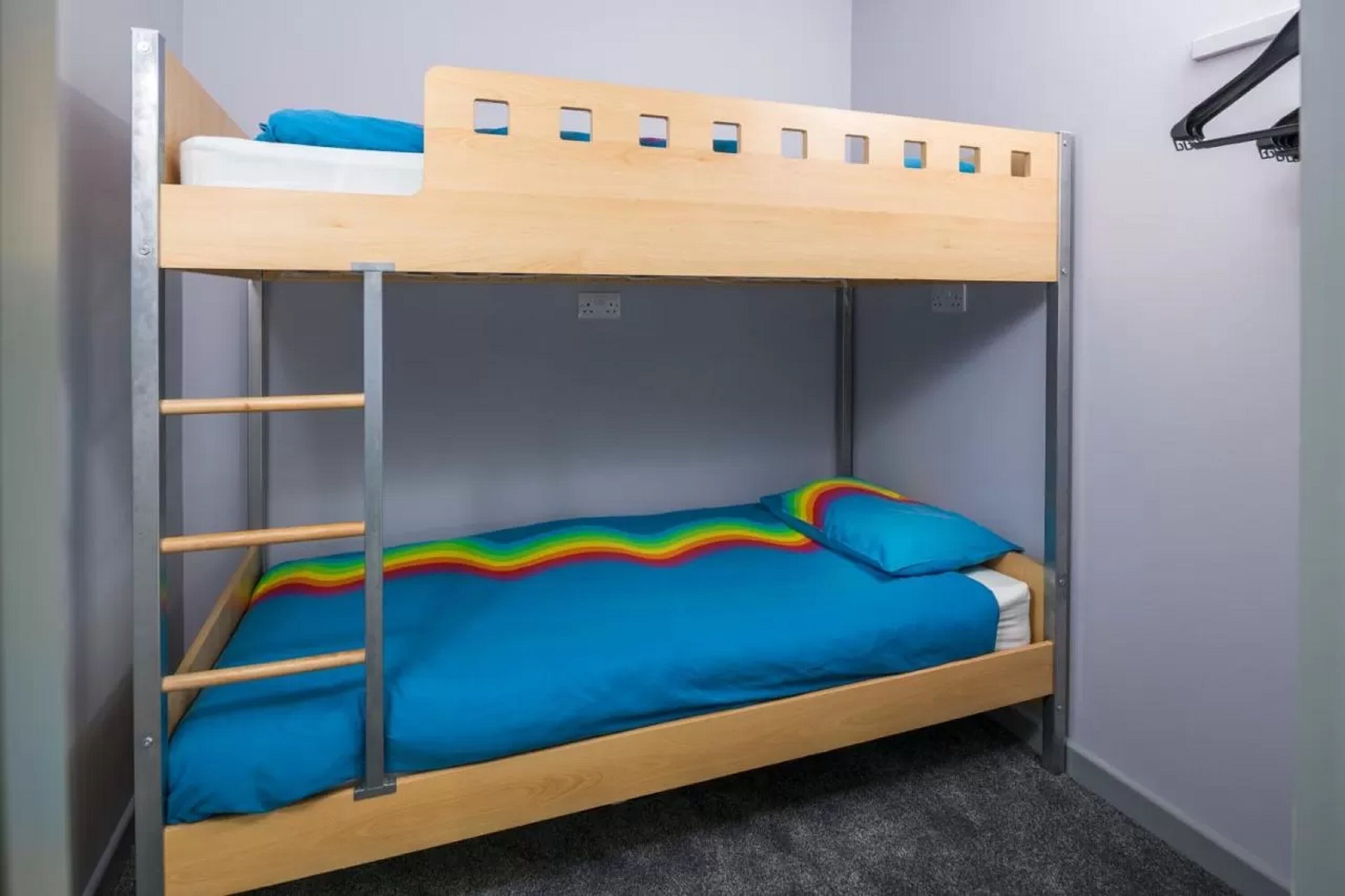 Una cama litera con un edredón estampado con motivos de arcoíris y una parte superior de madera.