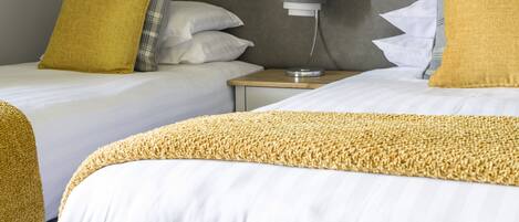 A hotel room with two beds, a bedside table, and a lamp.