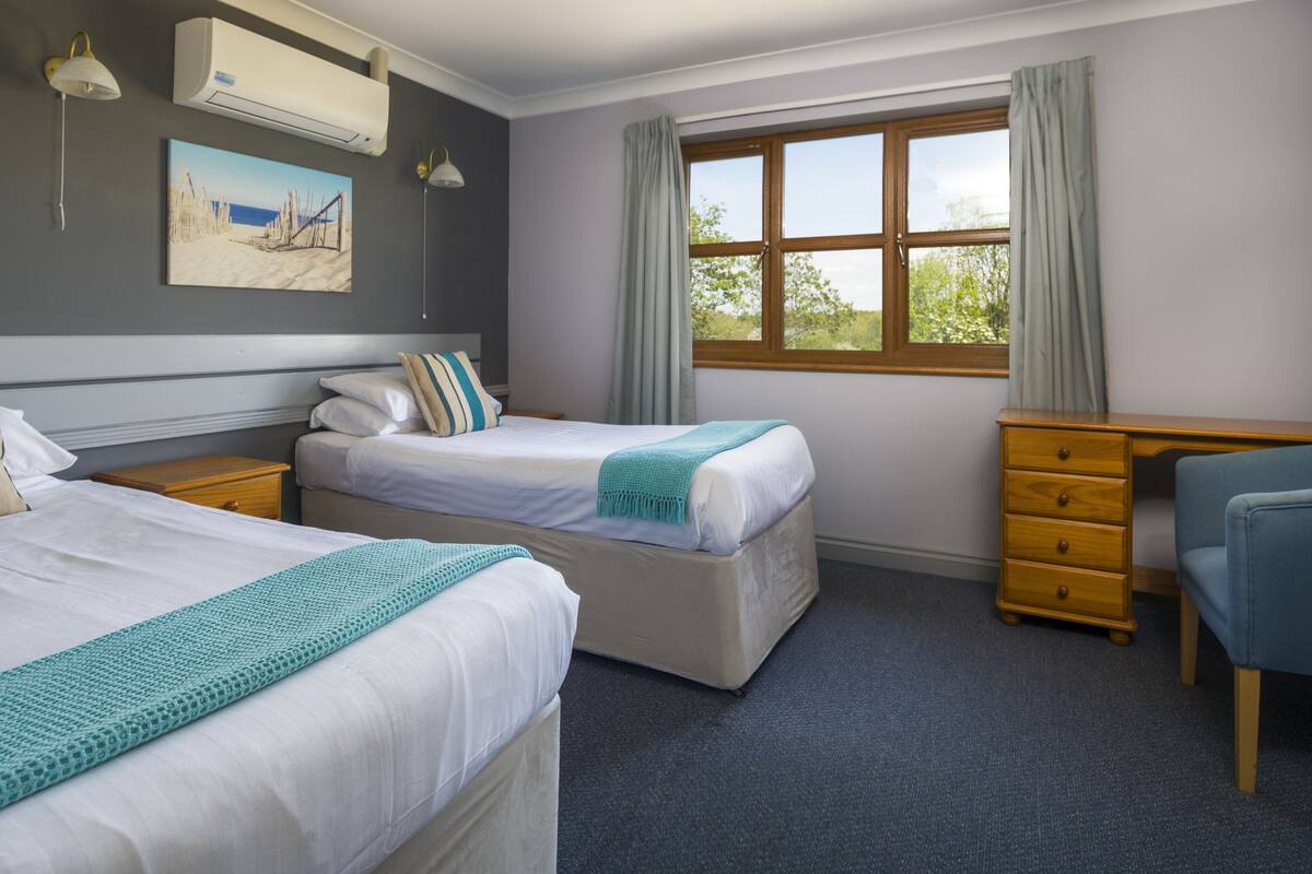 A hotel room with two beds, a dresser, a desk, and a window with curtains.