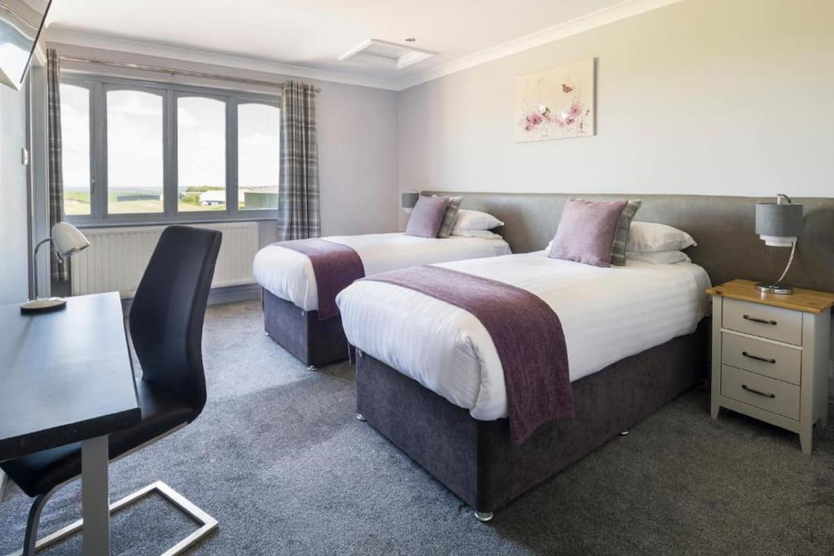 A hotel room with two beds, a desk, and a chair.