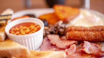 A breakfast plate with toast, beans, bacon, sausages, and a small bowl of sauce.