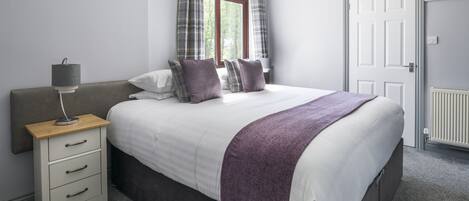 Et soveværelse med seng, et natbord med lampe, et vindue med gardiner og en dør.