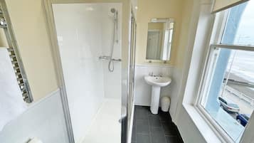 Un baño con ducha de vidrio, lavamanos, espejo y ventana con vista al mar.