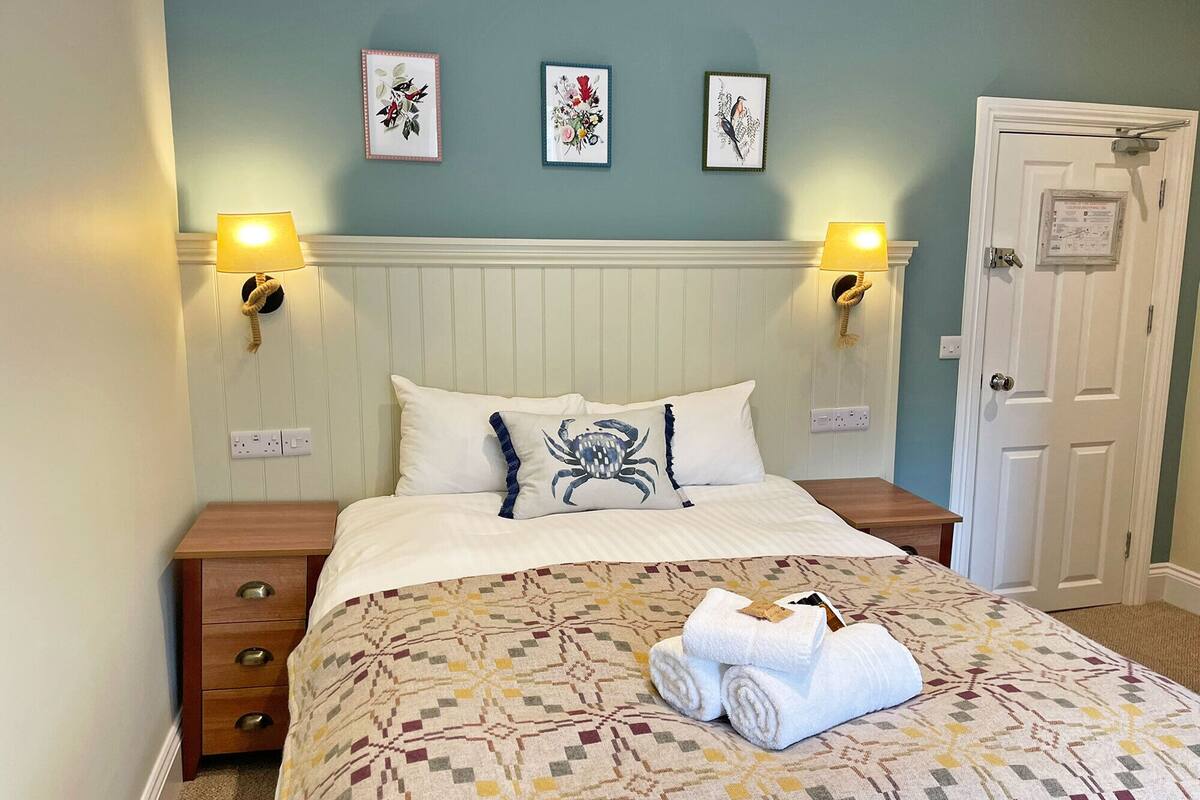 A neatly made bed with a patterned bedspread, two wall-mounted lamps, and three framed artworks on the wall.