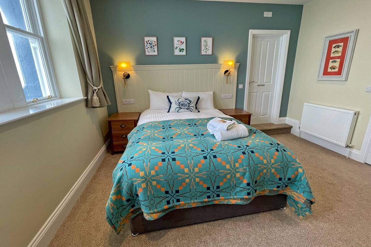 A neatly arranged bedroom with a bed, two bedside tables, a window with curtains, and wall-mounted lamps.