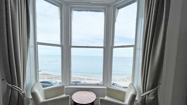 A bay window with two chairs and a small table, overlooking a beach and the ocean. - The Glengower (Aberystwyth)