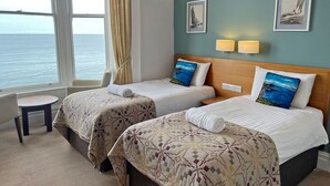 A hotel room with two beds, a small table, and a view of the sea. - The Glengower (Aberystwyth)