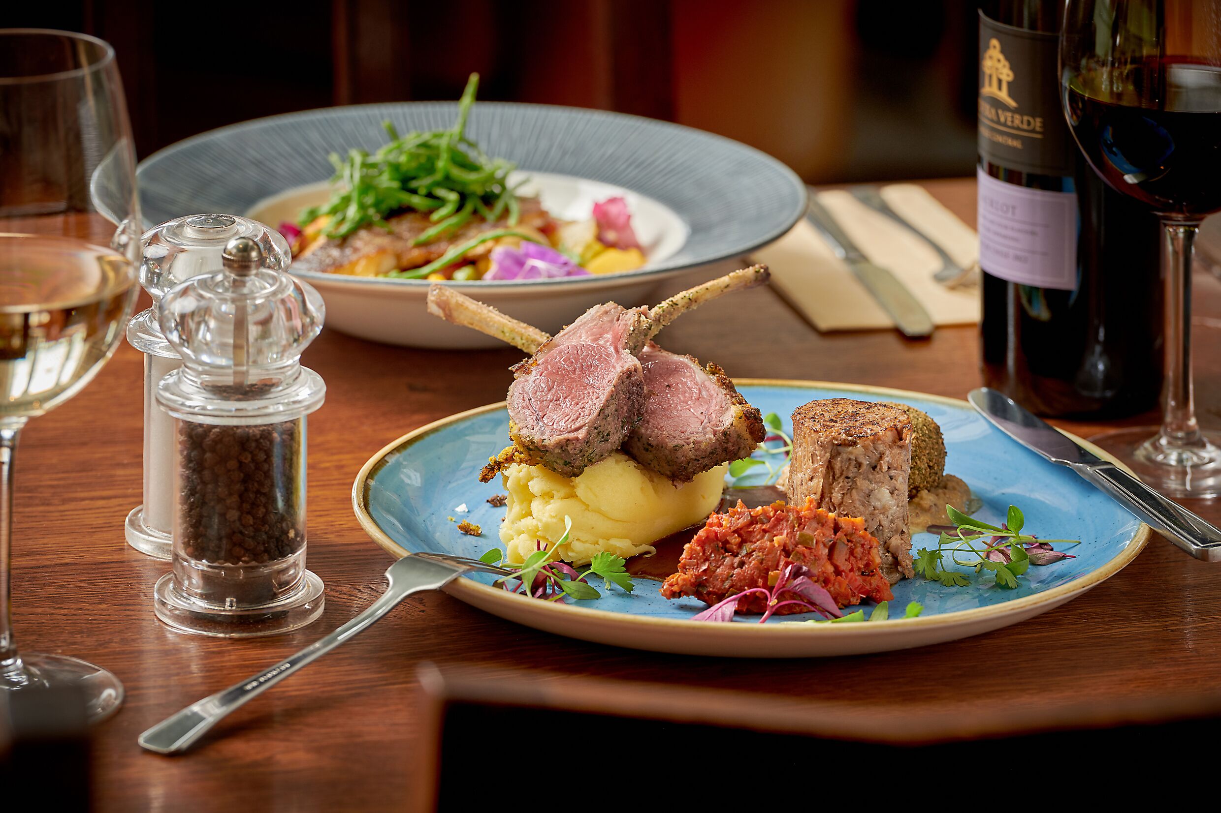 Una mesa de comedor con platos de comida, una botella de vino y un salero y pimentero.