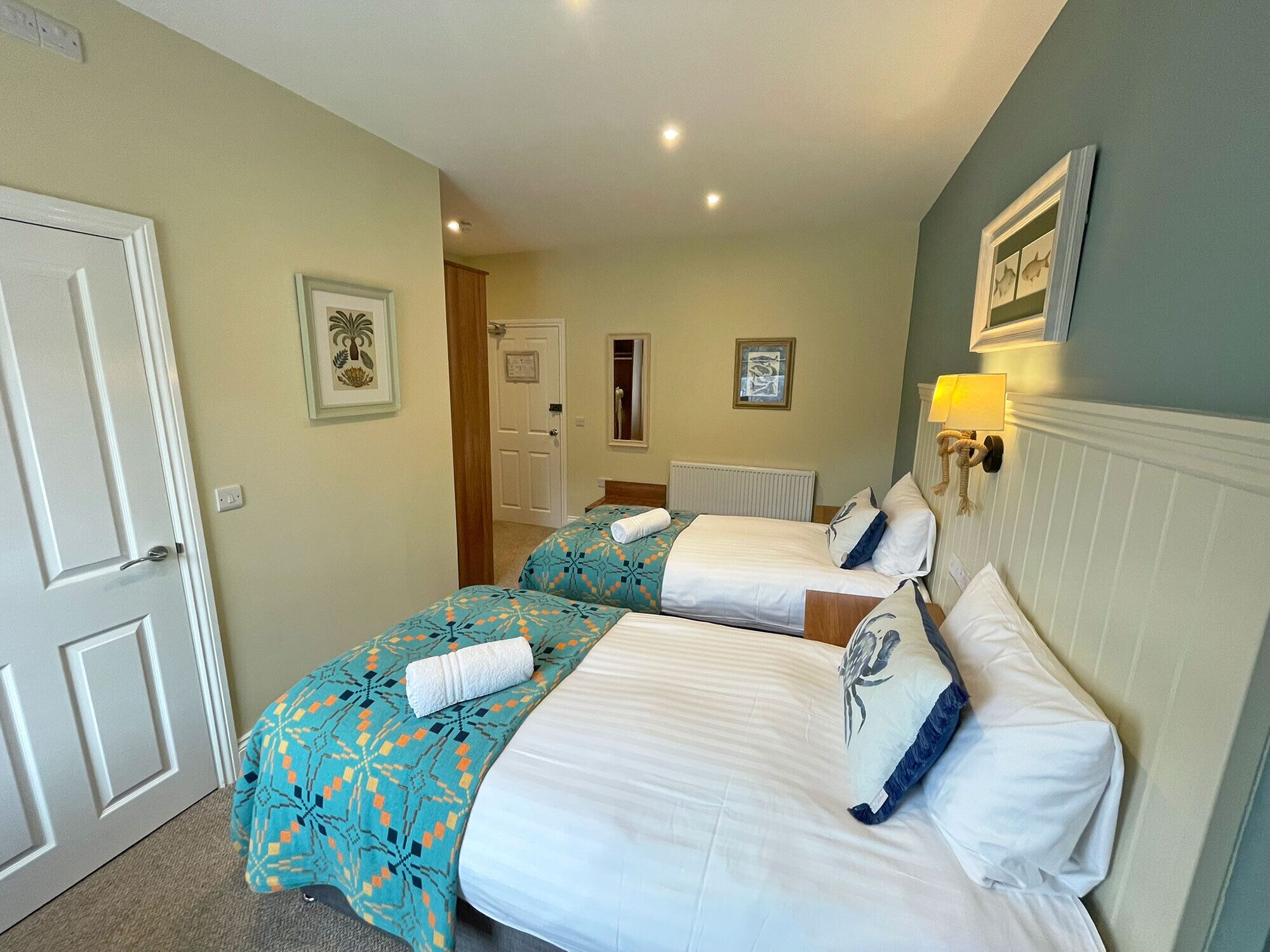 A hotel room with two beds, a door, a hallway, and a wall with a framed picture.