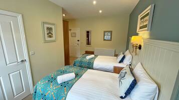 A hotel room with two beds, a door, a hallway, and a wall with a framed picture.