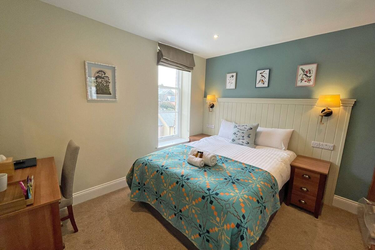 A bedroom with a bed, bedside lamps, a desk with a chair, and a window with a view.