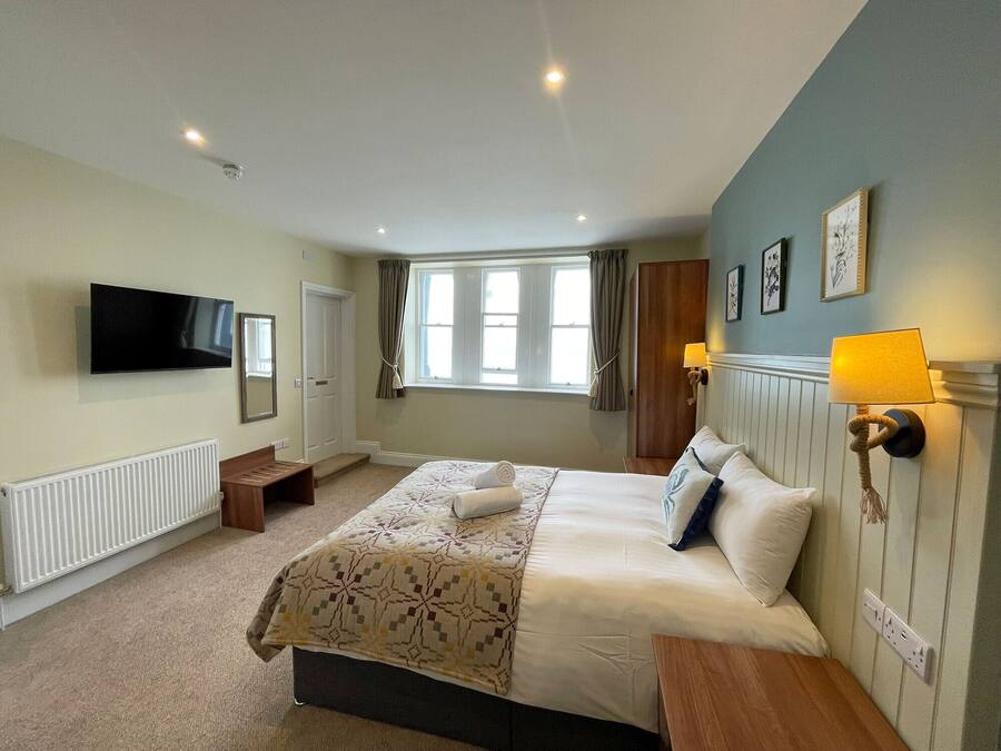 A hotel room with a bed, bedside table, lamp, and a television on the wall.
