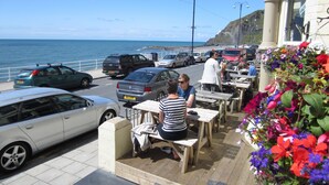 A coastal area with parked cars, outdoor seating, and a view of the sea. - The Glengower (Aberystwyth)