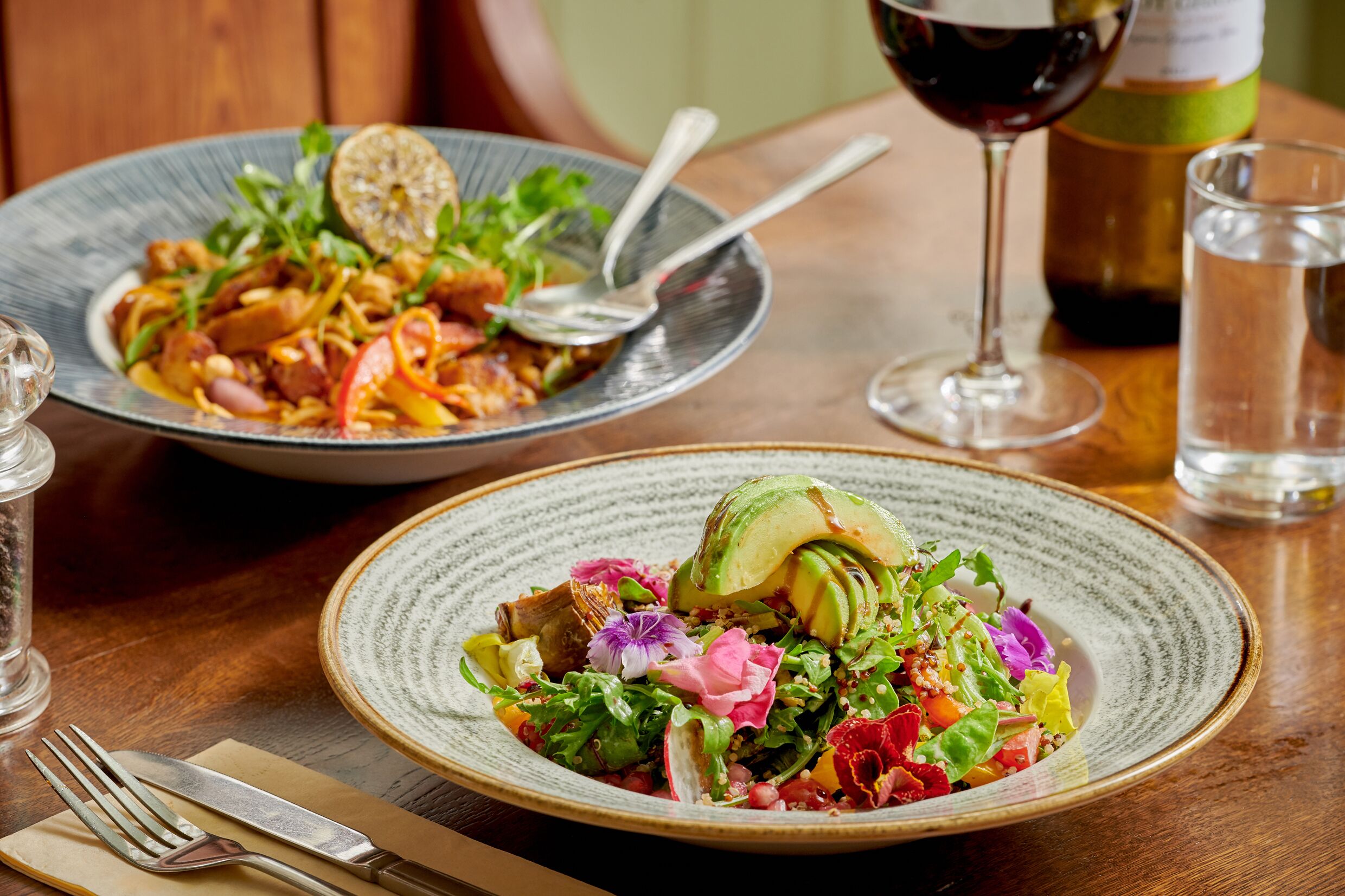 A dining table with two plates of food, a wine glass, and a bottle of wine.