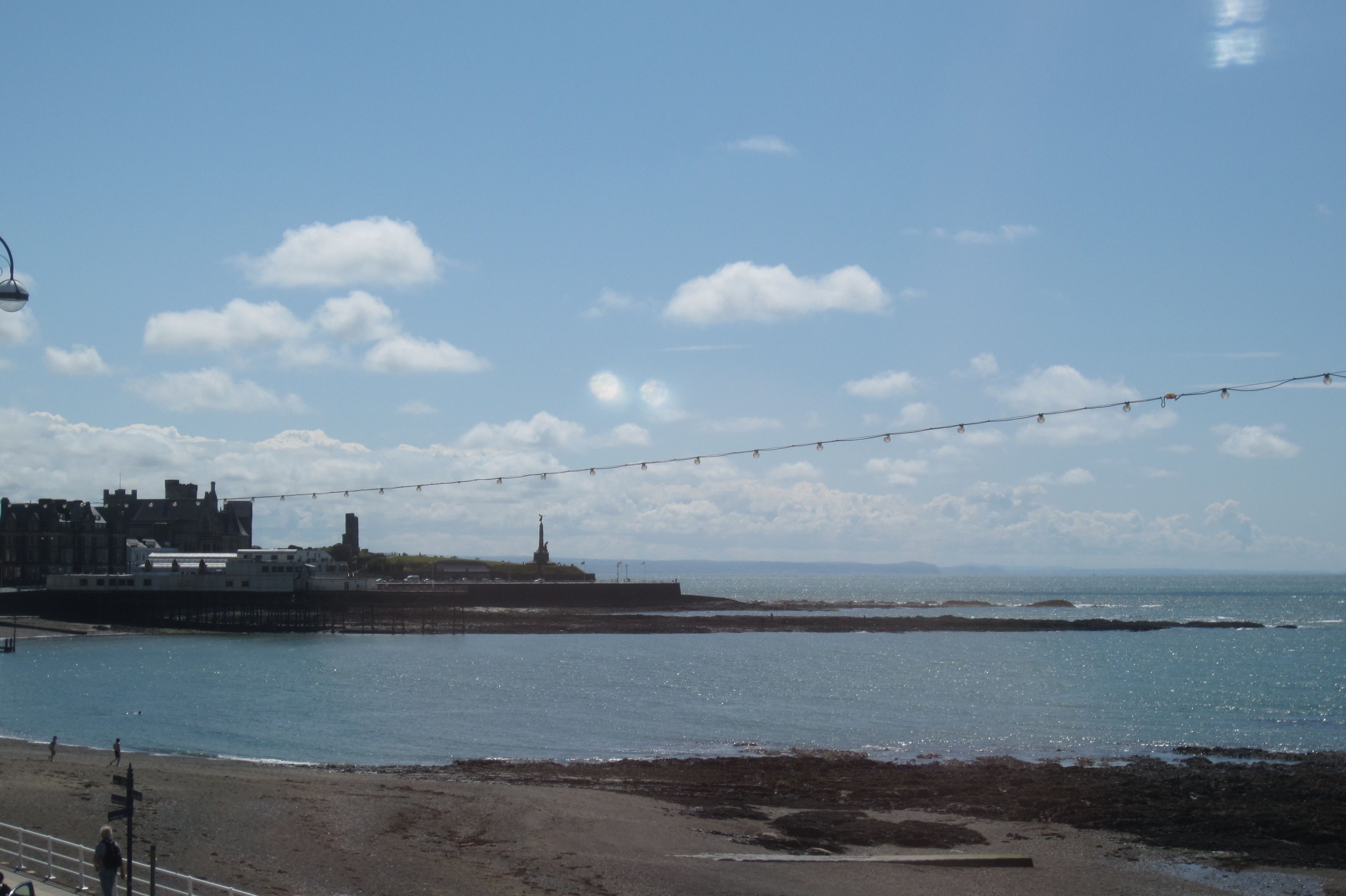 A coastal view with a pier, beach, and buildings in the background.