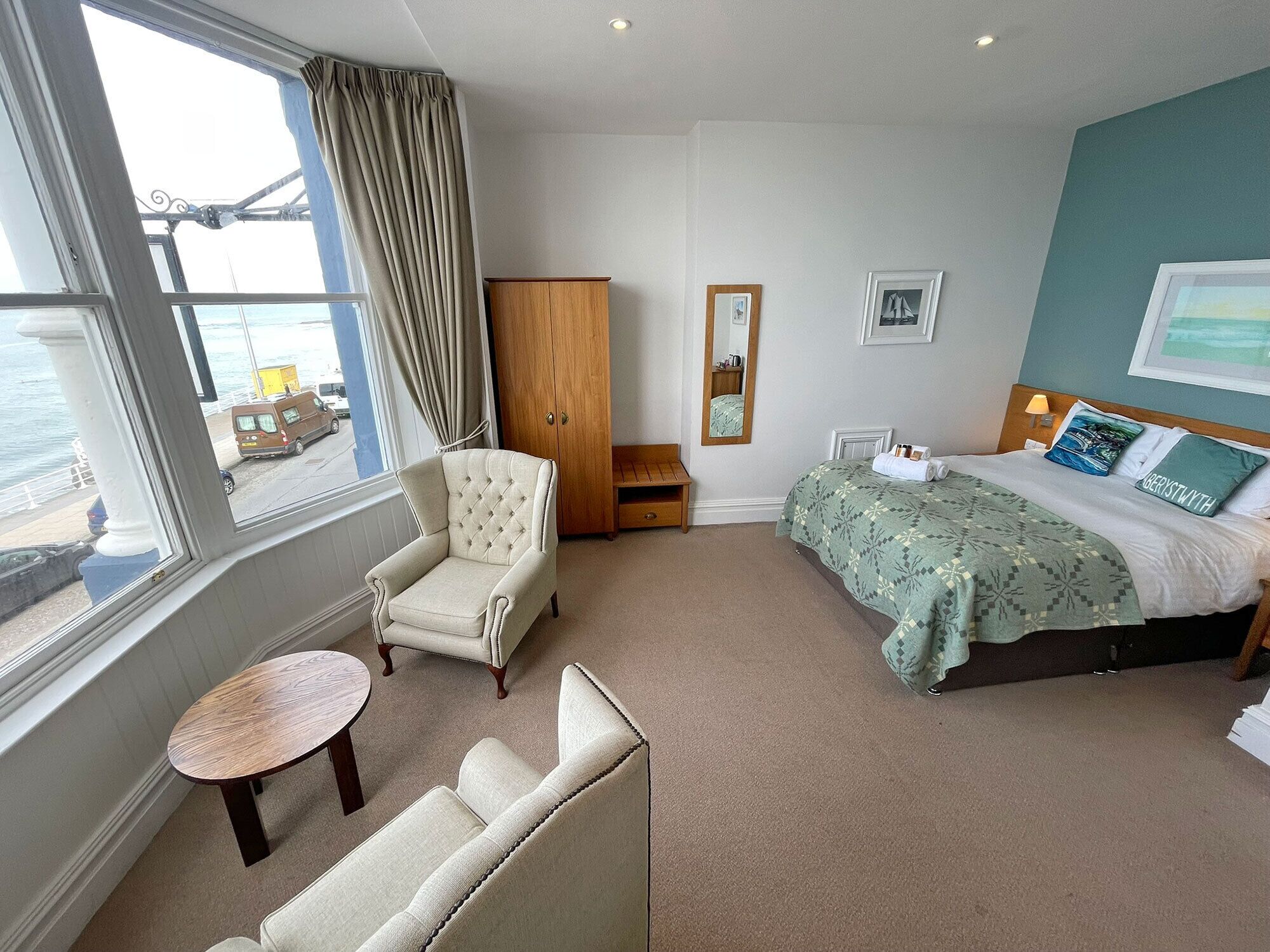 A hotel room with a bed, a chair, a small table, and a wardrobe.