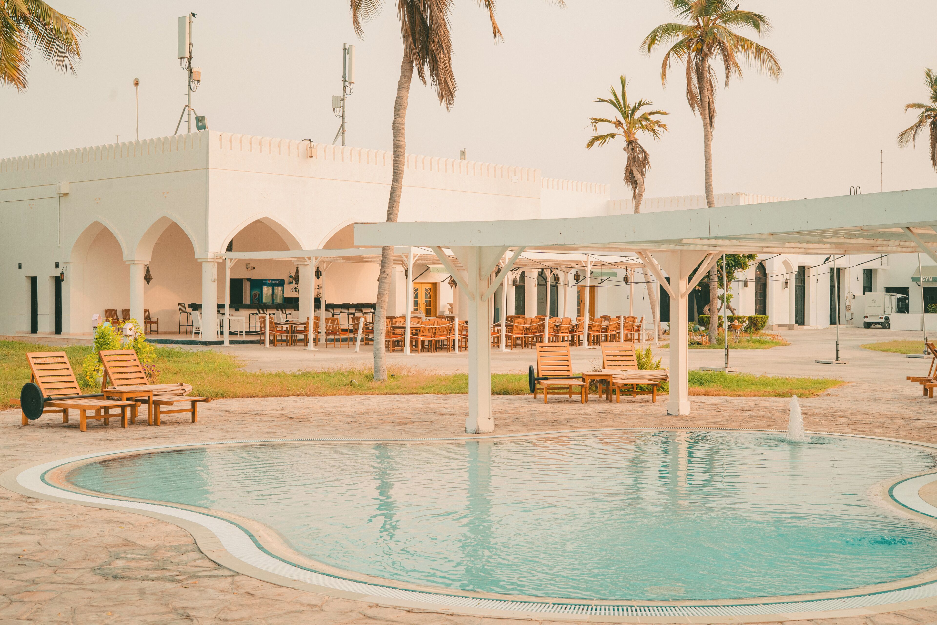 A swimming pool with lounge chairs, a covered seating area, and palm trees.