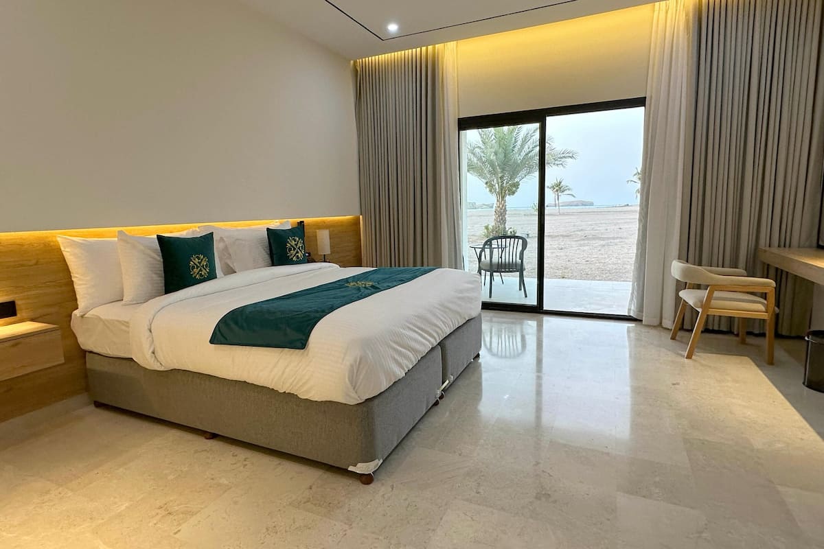 Ein modernes Hotelzimmer mit einem großen Bett, einem Schreibtisch und Blick auf den Strand.