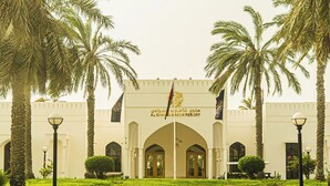 La entrada al Al Sawai Beach Resort, con palmeras y un cielo despejado.