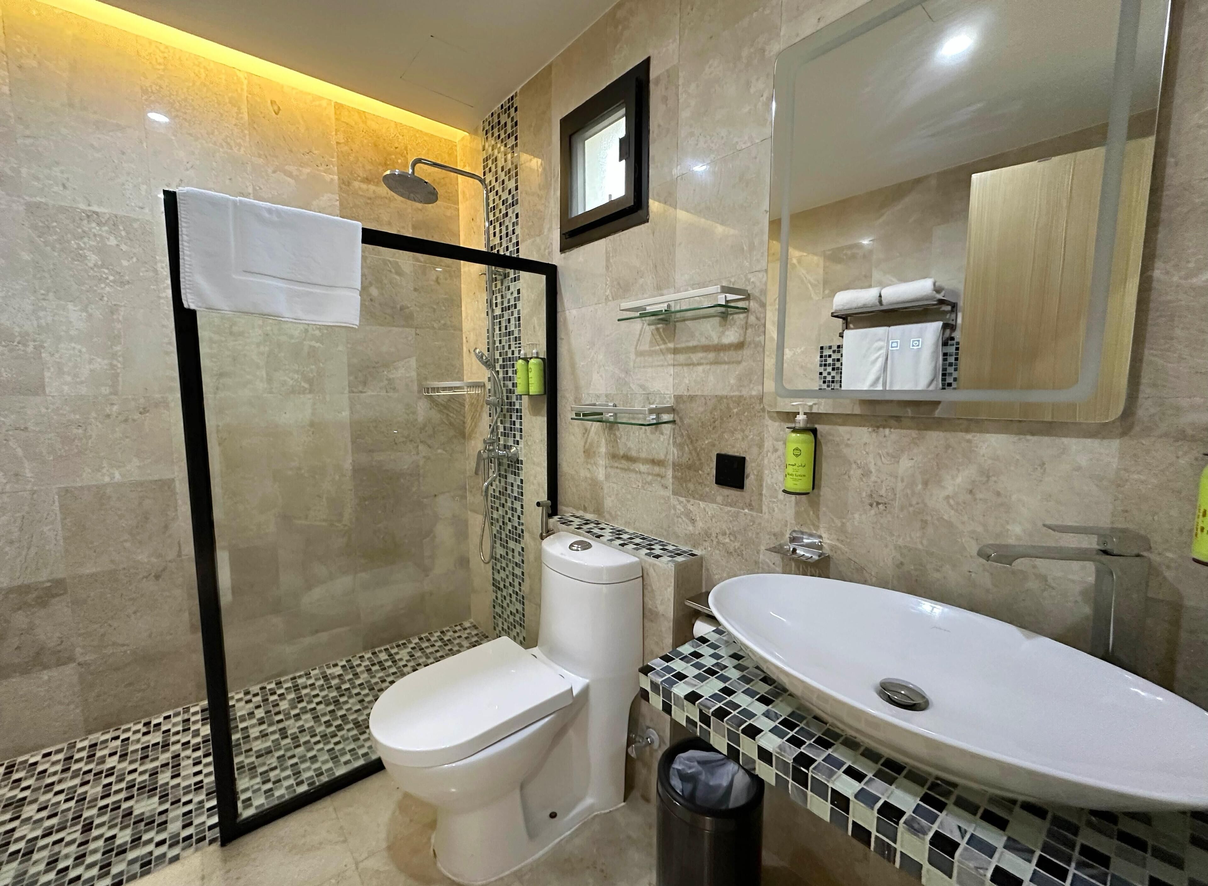 A modern bathroom with a glass-enclosed shower, a white toilet, a sink with a mosaic tile countertop, and a mirror above the sink.