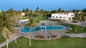 Un resort con una amplia piscina central, palmeras y zonas de estar al aire libre.
