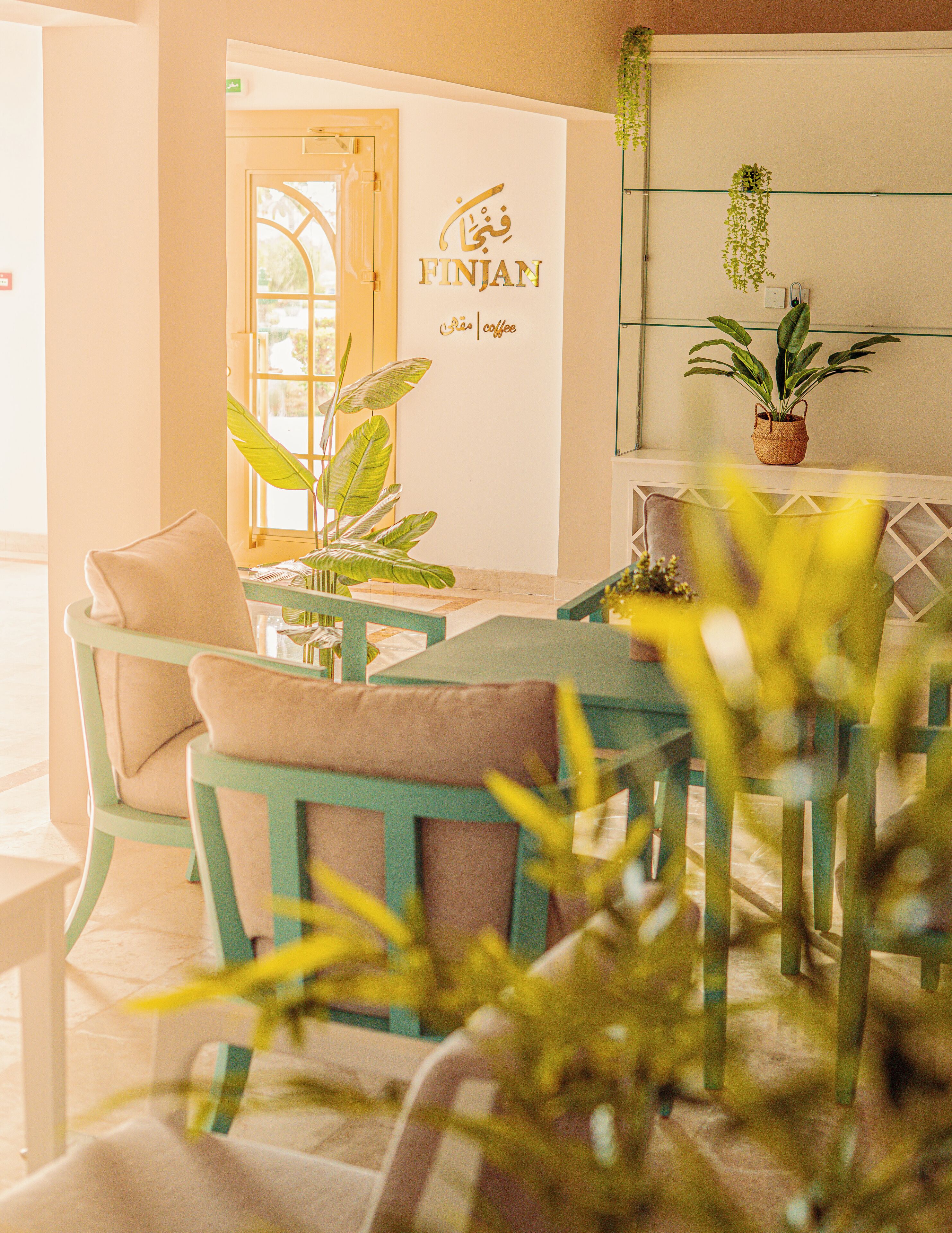 A cozy seating area with a table and chairs, a potted plant, and a wall with a logo and text.