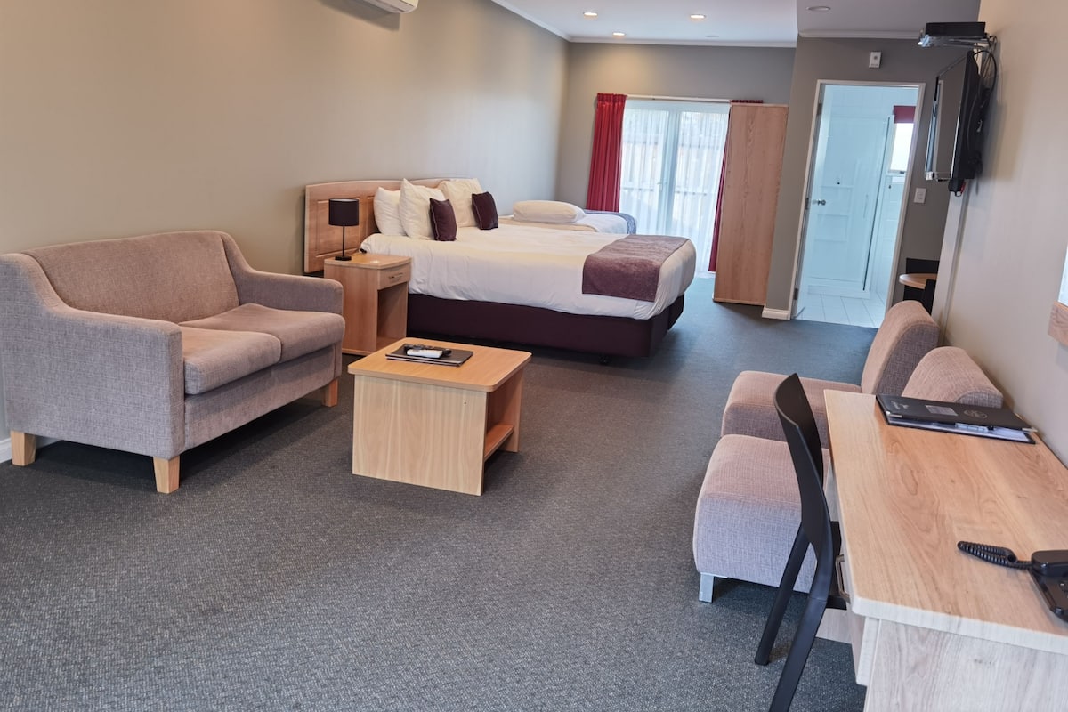 Ein Hotelzimmer mit einer Couch, zwei Einzelbetten, einem Schreibtisch und einem Fernseher.
