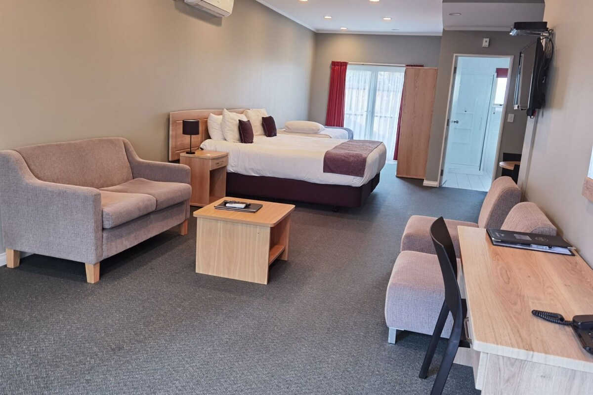 A hotel room with a sofa, a bed, a desk, and a television.