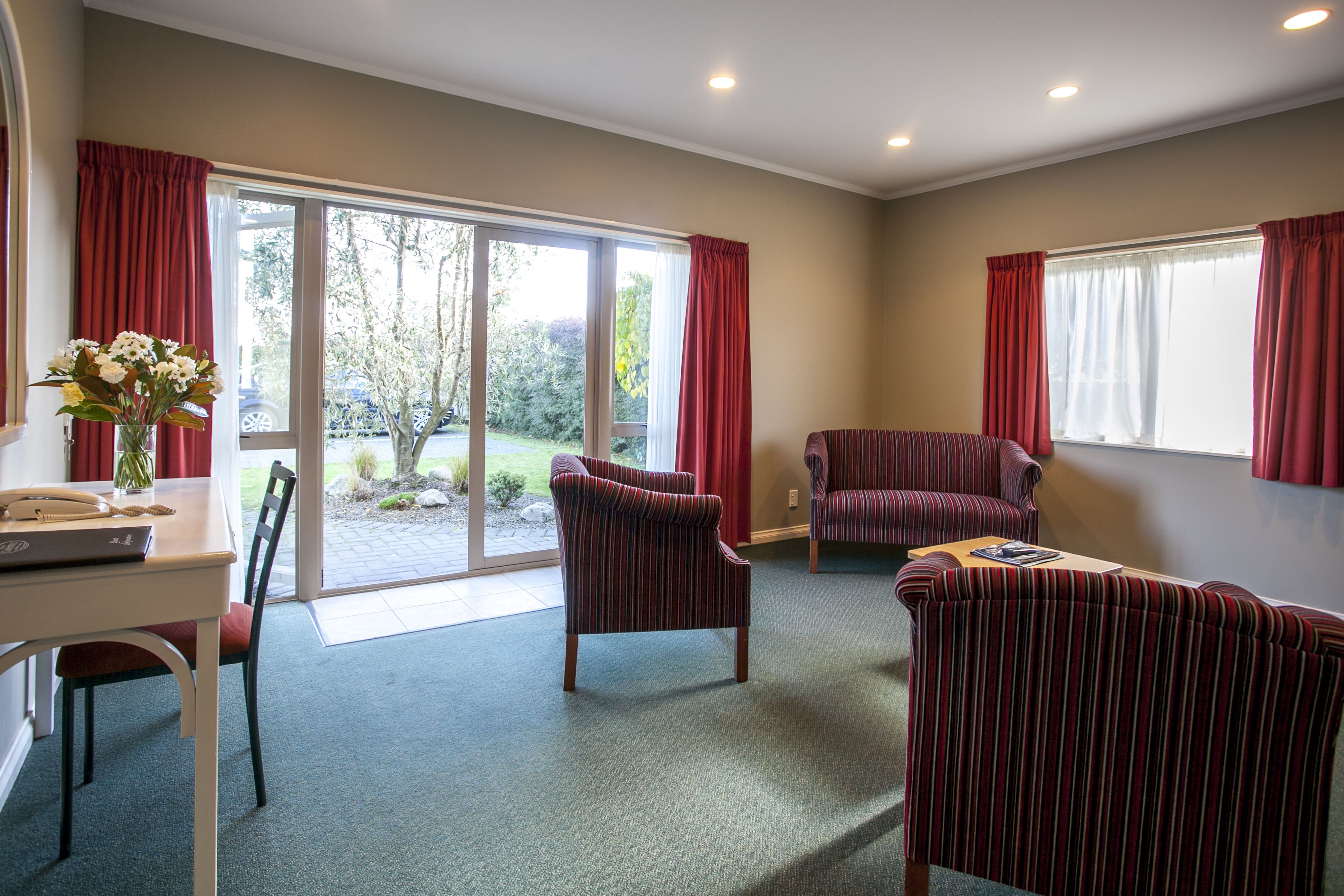 A spacious room with a dining table, two striped armchairs, a sofa, and a large sliding glass door leading to a garden.