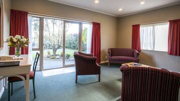 A spacious room with a dining table, two striped armchairs, a sofa, and a large sliding glass door leading to a garden.