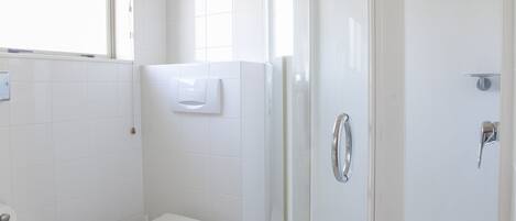 A modern bathroom with a glass-enclosed shower, a toilet, and a window with a red valance.