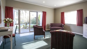 A room with a dining table, two striped armchairs, a sofa, a TV, and a large window with curtains.